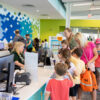 Children happily crowd the children's desk to sign up for Summer Reading 2026.