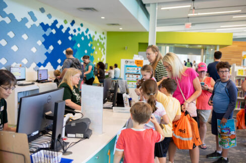 Children happily crowd the children's desk to sign up for Summer Reading 2026.
