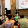 Author sits at the head of the room speaking out to a crowd of families.
