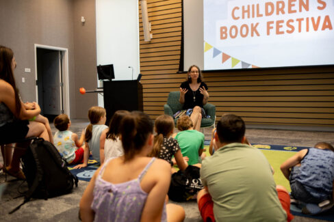 Author sits at the head of the room speaking out to a crowd of families.