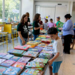 Librarians assist families pick children's books from a table.
