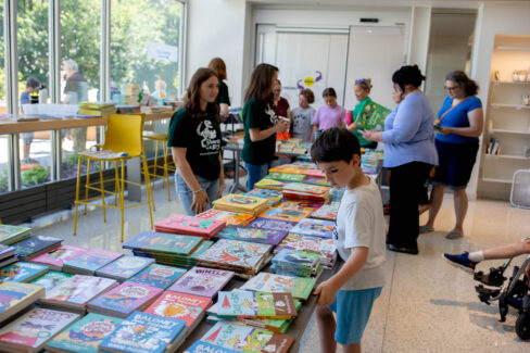 Librarians assist families pick children's books from a table.