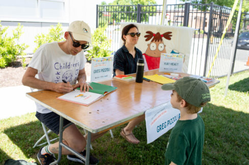 Little kid stands as author autographs a children's book.